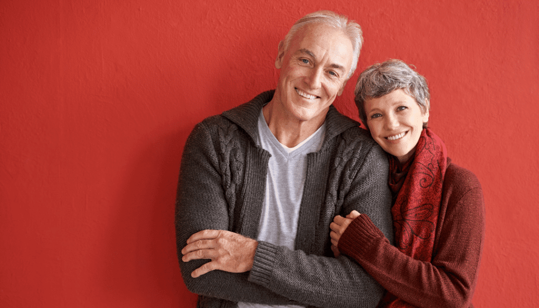 Smiling couple posing against red wall.